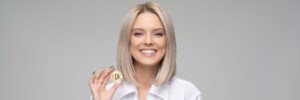 Millennial blond woman in a white shirt holding a bitcoin and smiling.